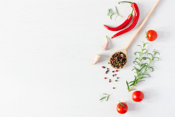 Composition of colorful pepper seeds, fresh chili pepper, tomatoes, garlic and rosemary herb top view on white wooden background. Italian herbs and spices.