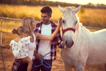 Family of three bonding with a white horse.  Fun on countryside, sunset golden hour. Freedom nature...