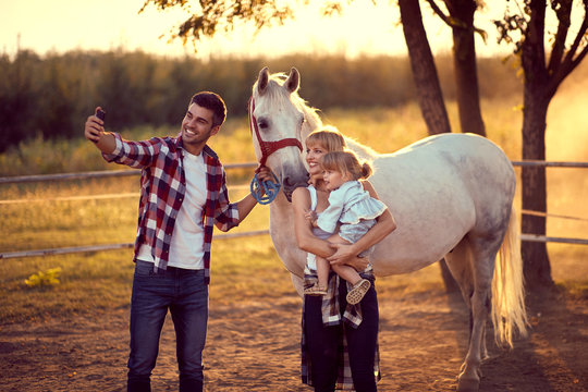 Dad taking a photo with faily and a horse. Family on countryside, sunset golden hour. Freedom nature concept.