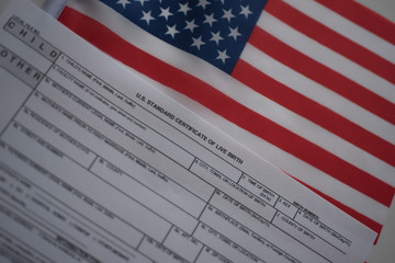 U.S. standard certificate of live birth application form next to flags of USA. Birthright citizenship concept. Diagonal view.