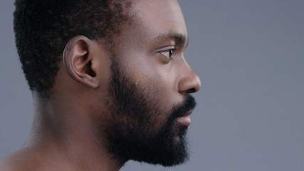 Profile of attractive topless emotionless afro-american young man standing straight looking forward isolated on dark background.