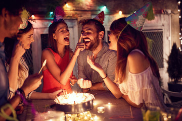 Smiling group of young friends having birthday party in the club with cake and candles at night. Party, fun, birthday concept.