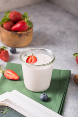 Organic probiotic milk kefir drink or yogurt in glass with strawberry, on the white grey background. Gut health. Fermented dairy beverage. Trendy food. Copy space