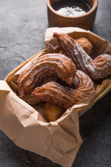 Churros in a paper bag with sugar and chocolate sauce on black background. top view.