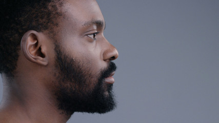 Obraz premium Profile of attractive topless emotionless afro-american young man standing straight looking forward isolated on dark background.