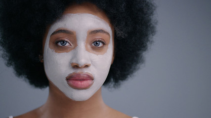 Adorable portrait of gorgeous african young woman having a white mask on her face. Charming beauty black model isolated on grey background. Facial treatment concept.