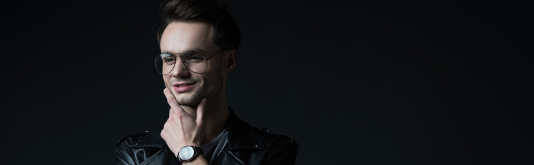 smiling dreamy stylish brutal man in biker jacket isolated on black, panoramic shot