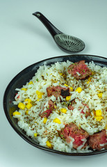 Dark porcelain bowl of white rice with corn, burger and oregano. And a black spoon.