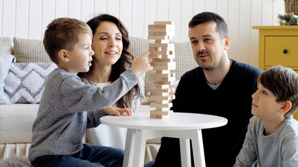 Family of four people is playing in board game with wooden tower together at home.