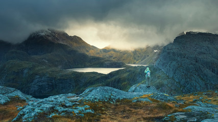 tourist photographs gaps of sunlight among thunderclouds on a trek on Mount Munken in Norway on the Lofoten Islands