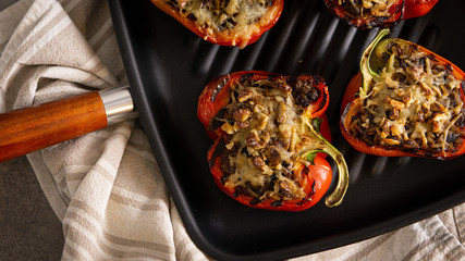 Oven baked red stuffed paprika with meat, cheese, nuts on a grill pan. There is striped towel on a background. 