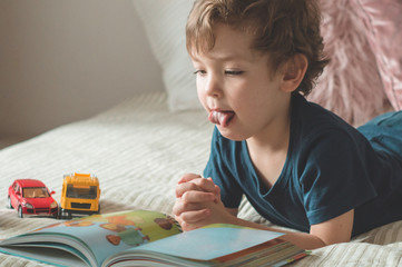 Child reading book. Kids read books. A little boy sits on a bed with your toys in living room...