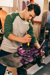 worker screwing snowboard binding to snowboard in repair shop
