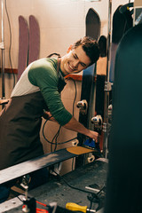 smiling worker waxing ski with wax iron in repair shop