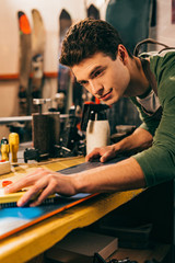selective focus of worker using brush on snowboard in repair shop