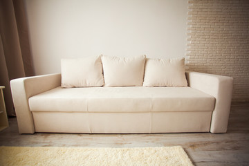 Beige sofa against white brick wall with copy space.