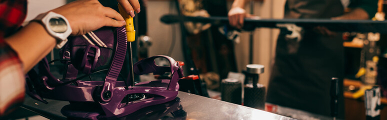 panoramic shot of worker screwing snowboard binding to snowboard in repair shop