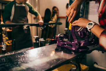 cropped view of worker screwing snowboard binding to snowboard in repair shop