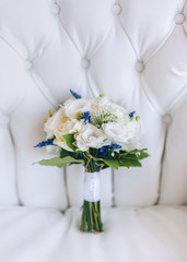 Beautiful and stylish wedding bouquet with white roses lies on the background of a light gray sofa. Wedding details and decorations. Flowers for the bride.