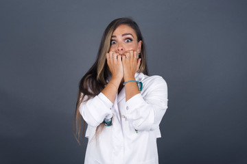 Anxiety. beautiful young caucasian doctor woman covering her mouth with her hands and standing indoors. Scared from something or someone bitting nails.
