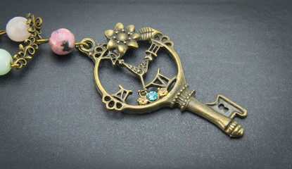 A jewelry on a chain in the form of a brass-colored key with beads on a black background.