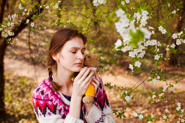 Fototapeta premium Teenage girl huggs toy bear in spring garden. Beautiful sad girl face with freckles.