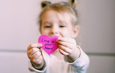Portrait of a happy smiling little girl holding handmade valentine. Heart in the arms. Symbol of love. Valentine's concept. Happy childhood