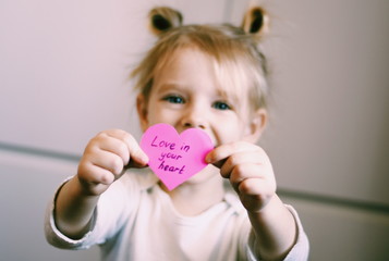 Portrait of a happy smiling little girl holding handmade valentine. Heart in the arms. Symbol of love. Valentine's concept. Happy childhood
