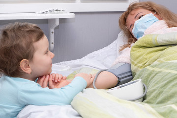 The woman is sick, lies on the bed. The child holds mother by the hand and sympathizes. Tonometer,...
