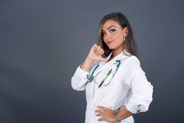 Closeup of cheerful beautiful European brunette young doctor woman looks joyful, satisfied and confident, points at herself with thumb, isolated over gray studio background.