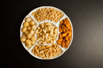 Assortment of various nuts on a white plate over black background.
