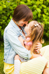 Happy mother and daughter hugging and kissing in summer park.