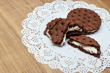 Fototapeta na wymiar A round shortbread biscuit with cream is broken into pieces and lies on a paper napkin with beautiful lace edges. Dessert for tea or coffee, children's treat.