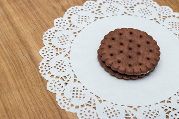 A round shortbread biscuit with cream lies on a paper napkin with beautiful lace edges. Dessert for tea or coffee, children's treat.