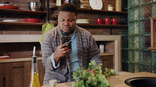 Close up face sad young african american man use phone sitting at kitchen coffee tea communication enjoyment relaxed cute breakfast food indoors morning portrait. - Powered by Adobe