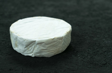 A whole head of Camembert cheese on a black background. Copy space.