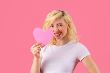 Studio portrait of a smiling young woman holding pink heart, romantic love, dating and Valentine's Day concept