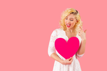 Studio portrait of a laughing young woman holding pink heart, looking down and gesturing, Valentine's Day love concept