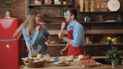 Attractive funny young loving couple dancing of joy cooking a tasty dinner in the kitchen at home. Fun home entertainment, cooking concept.