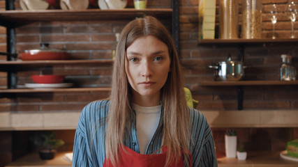 Amazing portrait of beautiful young woman looking at camera cooking dinner in the kitchen at home.