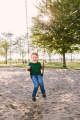 Happy smiling little preschool boy swinging on swingsat playground outside on summer day. Happy childhood lifestyle concept. Seasonal outdoor activity for kids.