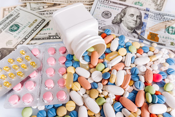 a lot of medical pills in different colors and capsules on a dollar bills, view from above