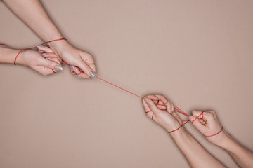 Top view of women pulling red string on beige background