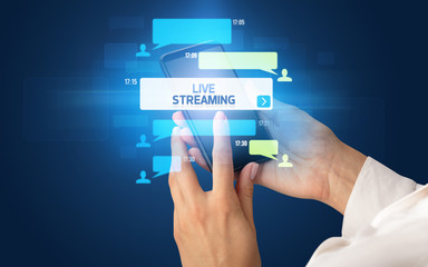 Female hand typing on smartphone with LIVE STREAMING inscription, social networking concept
