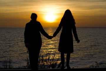 Girlfriends standing on railway rails holding hands on sunset background