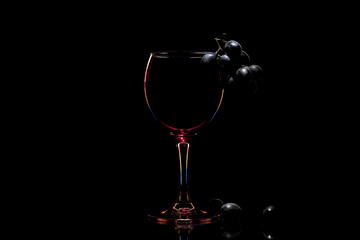 Wine glass with contour multicolored light. Black grapes and a glass on a black background with space for text.