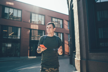 Pensive cool man with phone on city street in sunshine