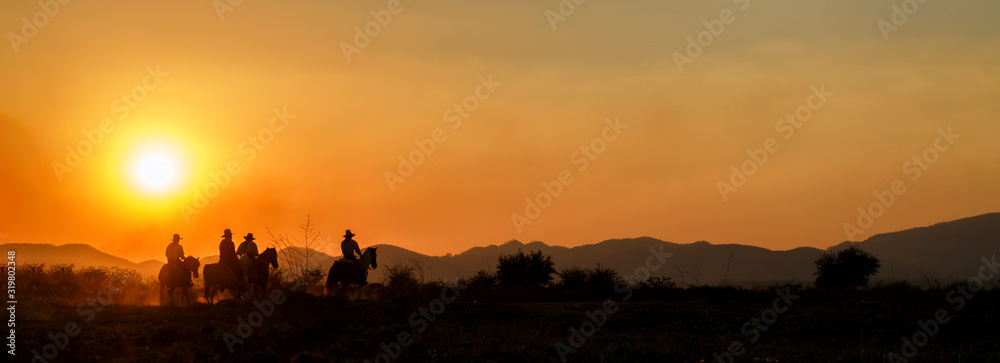 Wall mural Silhouette cowboy group riding horseback in farm at sunset, landscape panorama, banner