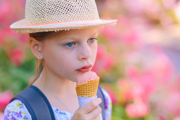 Little girl in a straw hat eating ice cream in a cone on a summer sunny day
