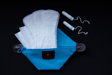 Critical days. Panty liners for menstruation, hygiene items - panty liners, panty liners and white tampons on a black background. Blue Hygiene Bag
